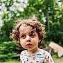 Louie is registered to the contest to win money with this photo: child, toddler, curly_hair, outdoor, greenery, nature, shirt, animal_print, portrait, face, cute, young, expression, daylight, casual_clothing, person, head, eyes, skin, background_blur