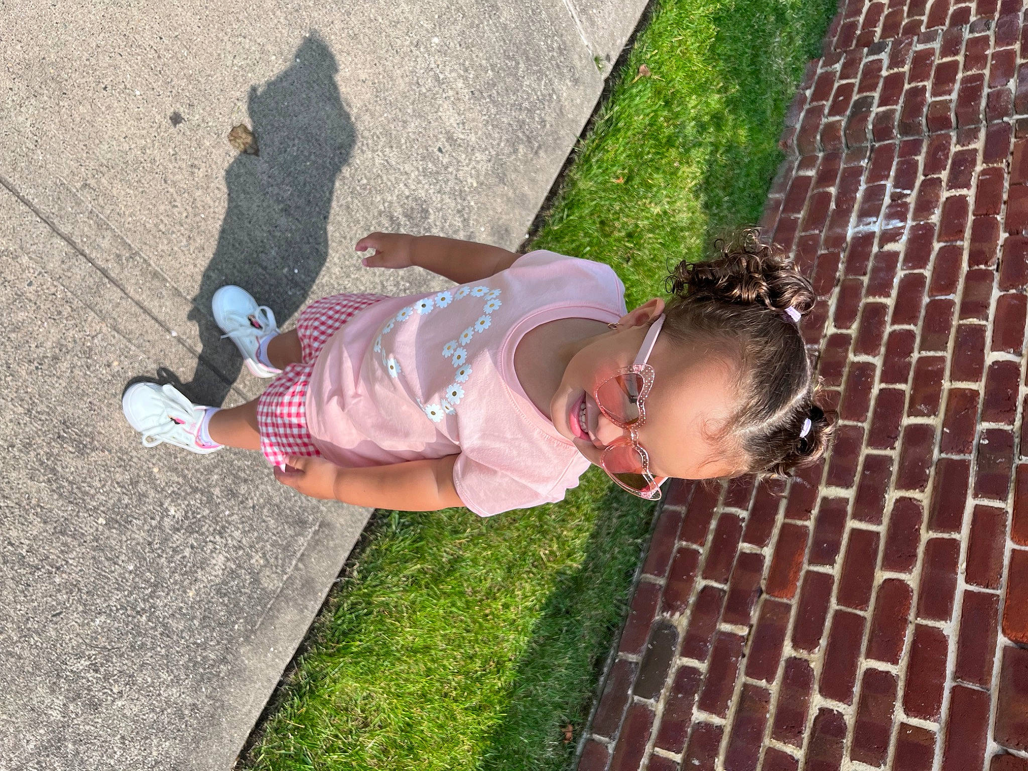 Kenzlee is registered to the contest to win money with this photo: asphalt, child, eyewear, flooring, fun, grass, happy, human_leg, leisure, pattern, people_in_nature, person, plant, recreation, road_surface, shadow, sidewalk, sunglasses, thigh, toddler