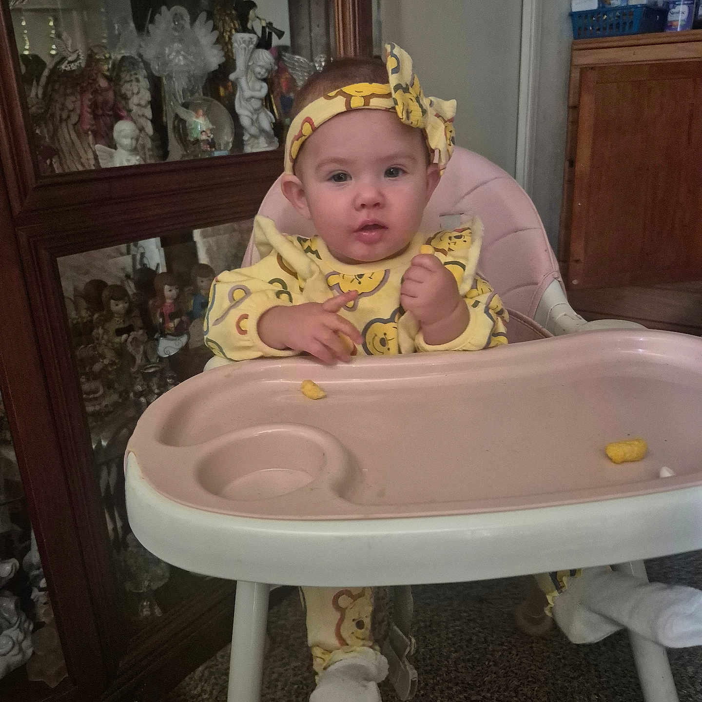 Serenity is registered to the contest to win money with this photo: baby, carpet, child, cute, decoration, dolls, expression, face, feeding, figurines, furniture, glass_cabinet, headband, high_chair, indoor, person, sitting, sock, toy, yellow_clothing
