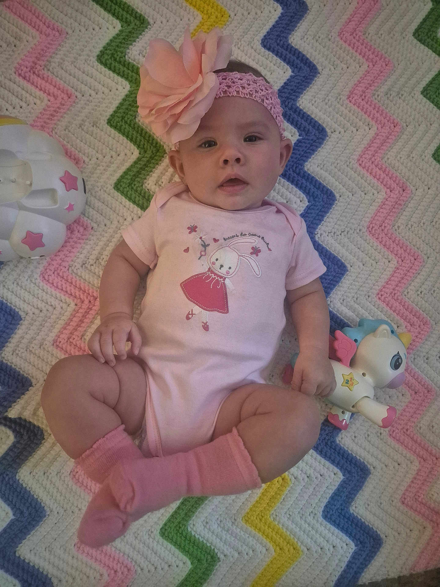 Serenity joined the competition — help win amazing prizes! baby, pink, headband, flower, toy, unicorn, blanket, zigzag_pattern, socks, onesie, infant, cute, child, lying_down, colorful, playful, indoors, soft_texture, happy, portrait