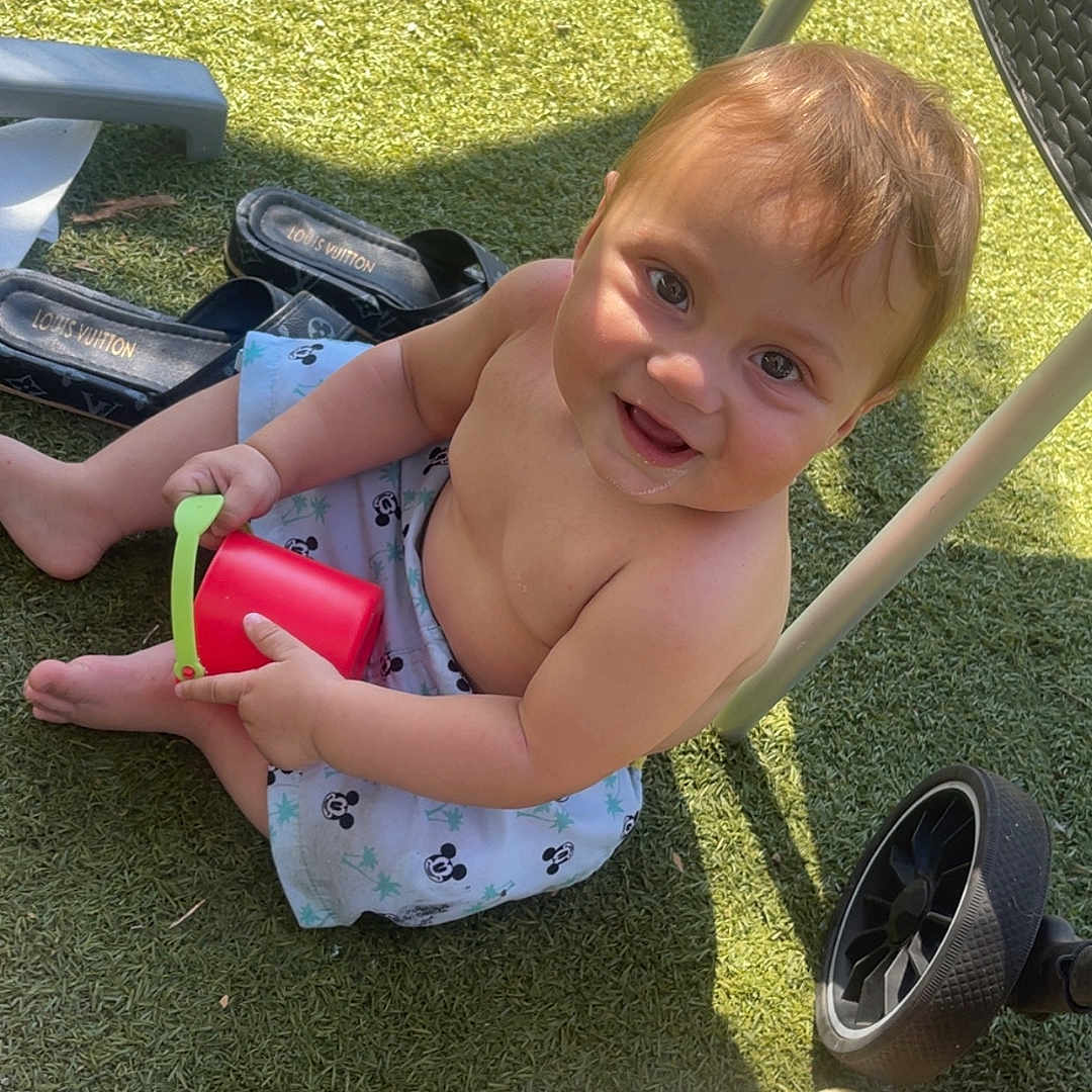 Mylan participe au concours pour gagner de l'argent avec cette photo : bare_chest, bucket, child, cute, grass, happy, outdoor, person, play, plush_toy, sandal, shadow, shorts, sitting, smiling, stroller, sunlight, toddler, toy, wheel