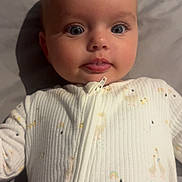 Hallie is registered to the contest to win money with this photo: baby, infant, face, eyes, tongue, onesie, clothing, sleepwear, cute, lying_down, soft_lighting, closeup, child, person, skin, head, expression, bed, fabric, zipped