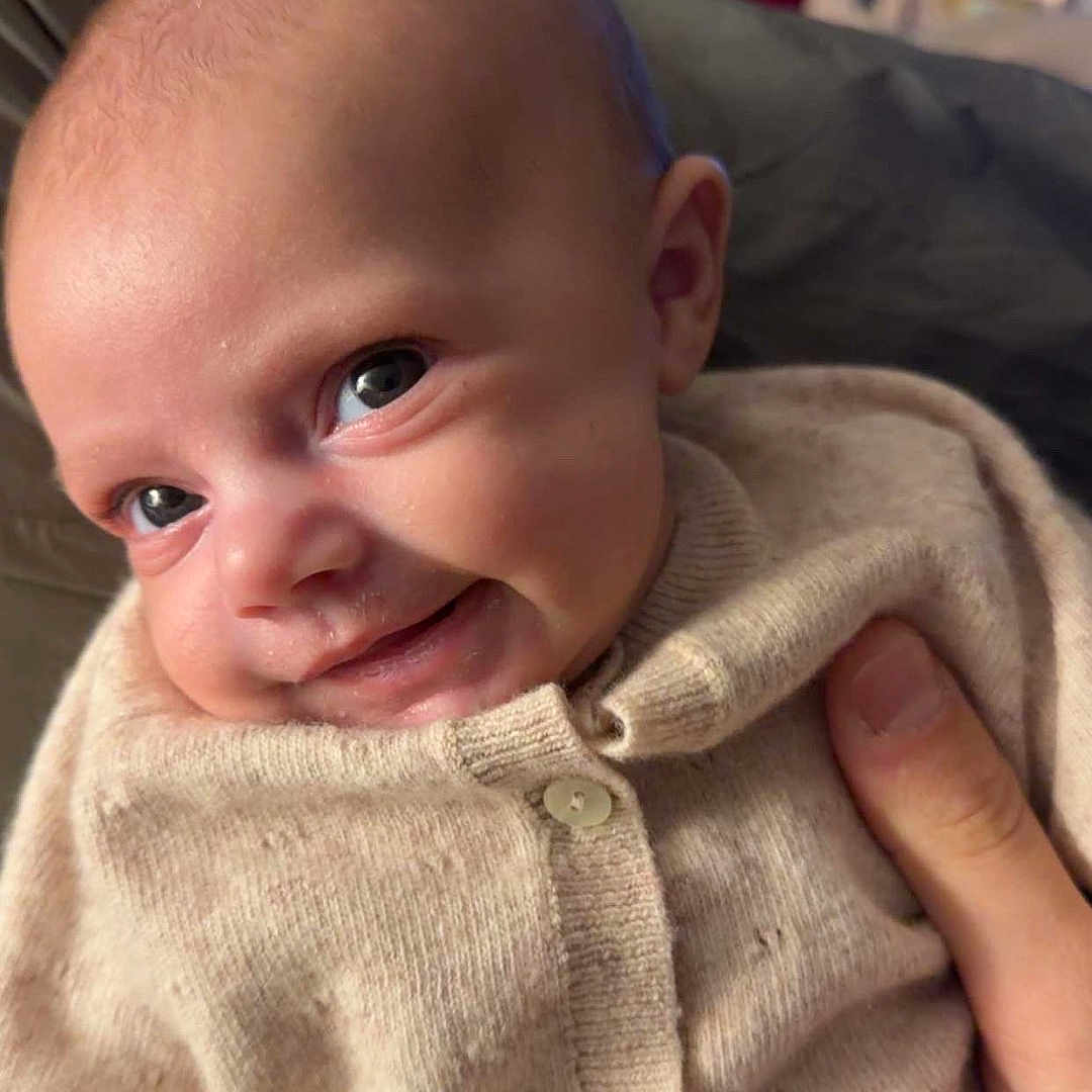 Basilia a rejoint le concours — aidez-le/la à gagner de superbes lots ! baby, beige_clothing, blurred_background, child, christmas_tree, closeup, cozy, cute, eyes, face, hand, holiday_decorations, indoor, infant, knitted_sweater, newborn, person, portrait, smiling, warm