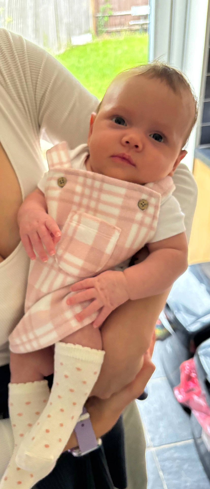 Indigo joined the competition — help win amazing prizes! adult_hand, baby, casual, child, close_up, curious_expression, cute, door, floor_tiles, holding, home, indoor, infant, patterned_clothing, person, pink_clothing, portrait, soft_lighting, white_socks, window