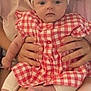 Louise participe au concours pour gagner de l'argent avec cette photo : baby, child, infant, person, adult_hands, checkered_dress, headband, flower, sitting, lap, smile, skin, closeup, indoors, soft_lighting, cute, young_child, holding, red, white