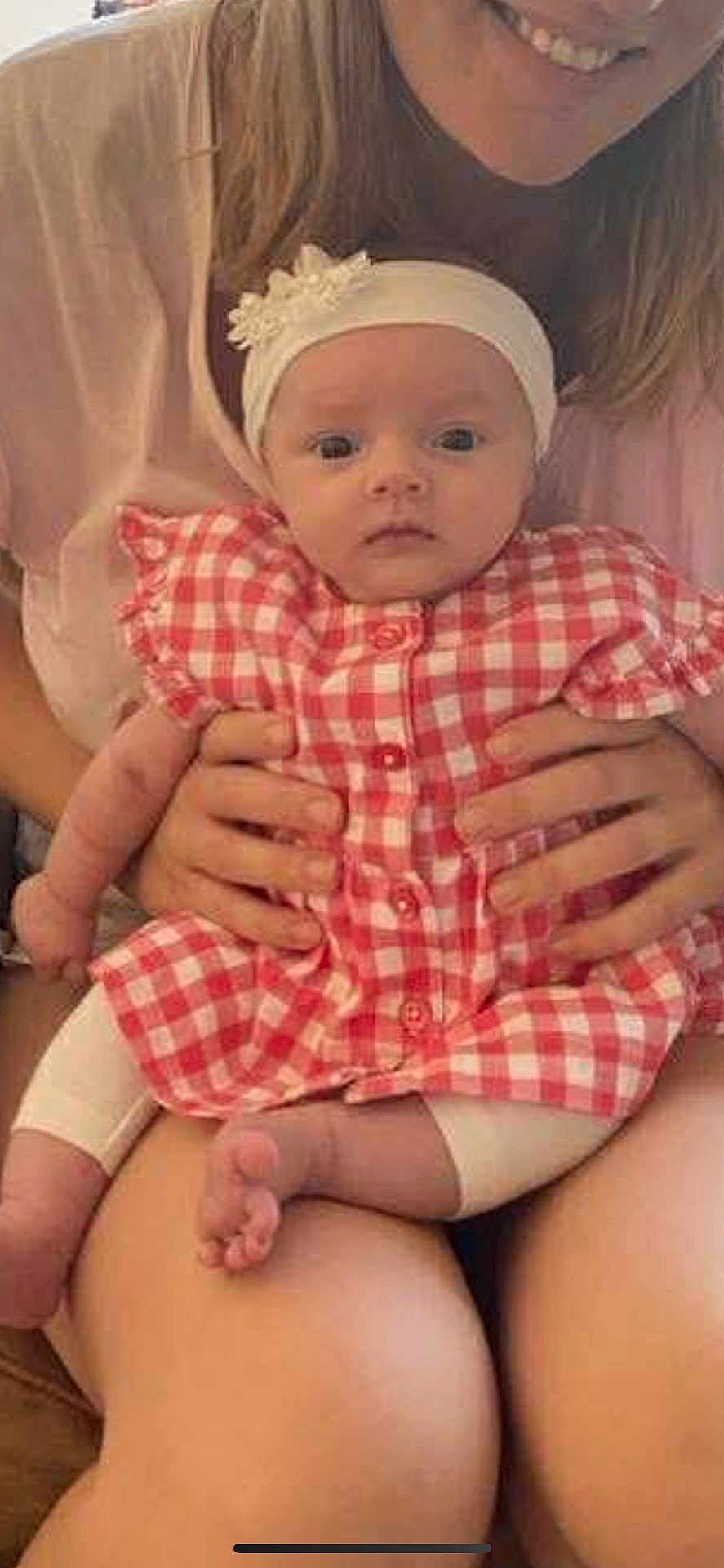 Louise participe au concours pour gagner de l'argent avec cette photo : baby, child, infant, person, adult_hands, checkered_dress, headband, flower, sitting, lap, smile, skin, closeup, indoors, soft_lighting, cute, young_child, holding, red, white