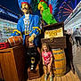 child, girl, statue, pirate, parrot, amusement_park, ferris_wheel, night, sign, wooden_floor, barrel, colorful, smiling, playland, outdoor, people, casual_clothing, footwear, rope, exhibit