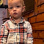toddler, child, curly_hair, plaid_shirt, indoor, wooden_wall, boxes, hands_in_pockets, standing, casual_clothing, portrait, young_child, curious, blond, person, jeans, expression, looking_at_camera, casual, cute