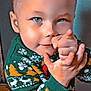child, toddler, boy, sweater, holiday_sweater, snowflake_pattern, pointing, blue_eyes, short_hair, smile, face, hands, portrait, indoor, wall, playful, festive, closeup, cozy, cheeky_expression
