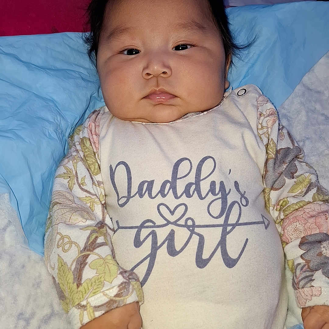 Kathleen Ann joined the competition — help win amazing prizes! baby, bed, blanket, child, chubby_cheeks, clothing, cute, expressionless, face, floral_pattern, hand, indoor, infant, lying_down, onesie, person, pillow, resting, sleepwear, text_on_clothing