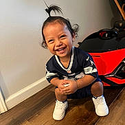 Lucca joined the competition — help win amazing prizes! toddler, child, smiling, squatting, indoor, toy_car, sports_jersey, white_shoes, wooden_floor, happy, cute, hair_ponytail, candid, person, floor, wall, bracelet, young_child, playful, home