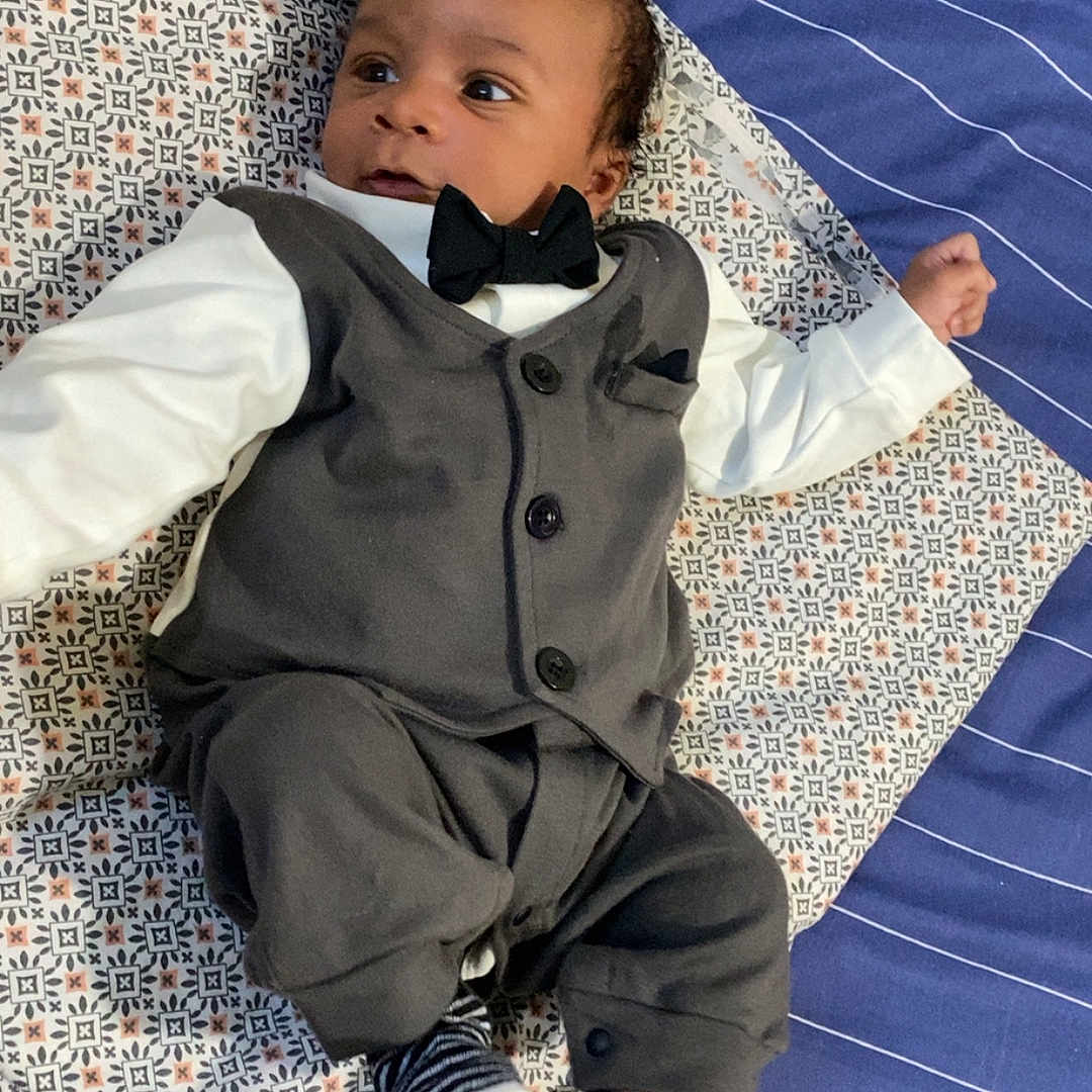 Djeylan participe au concours pour gagner de l'argent avec cette photo : baby, bed, black_hair, bow_tie, clothing, curious_expression, cute, fancy_outfit, indoors, infant, lying_down, patterned_pillow, person, portrait, small_socks, soft_lighting, striped_bedspread, striped_socks, tuxedo, young_child