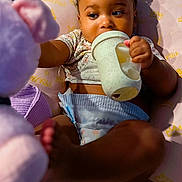 Amira joined the competition — help win amazing prizes! baby, child, diaper, sippy_cup, stuffed_animal, plush_toy, braids, cushion, indoor, cute, infant, reaching, relaxed, soft_lighting, portrait, young_child, comfort, casual_clothing, playful, toddler