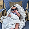 Eris is registered to the contest to win money with this photo: baby, blanket, blue_chair, child, cute, face, feet, fingers, footwear, infant, outdoor, person, portrait, relaxing, sunglasses, toddler, wrapped, young_child, seat, cozy