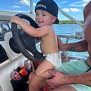 Frankie is registered to the contest to win money with this photo: adult, adventure, arm, boat, cap, child, clouds, diaper, fun, hand, happy, lake, outdoor, sky, smile, steering_wheel, summer, tattoo, toddler, water