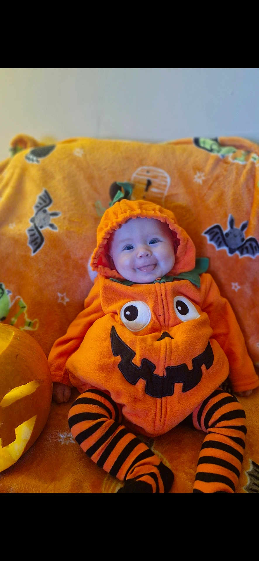 Esmae is registered to the contest to win money with this photo: baby, pumpkin_costume, halloween, carved_pumpkin, orange_blanket, smiling, tongue_out, striped_leggings, cute, holiday, festive, indoor, child, costume, jack_o_lantern, playful, happy, infant, seasonal, celebration