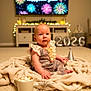 baby, infant, blanket, floor, carpet, mug, marshmallows, party_hat, balloons, 2026, fireworks, television, celebration, new_year, holiday, indoors, cozy, decorations, smiling, child