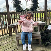 Malia joined the competition — help win amazing prizes! toddler, child, pink_jacket, jeans, white_sneakers, wooden_bench, gazebo, holiday_wreath, outdoor, smiling, happy, winter_clothing, railing, grass, trees, cloudy_sky, wooden_floor, person, cute, seasonal
