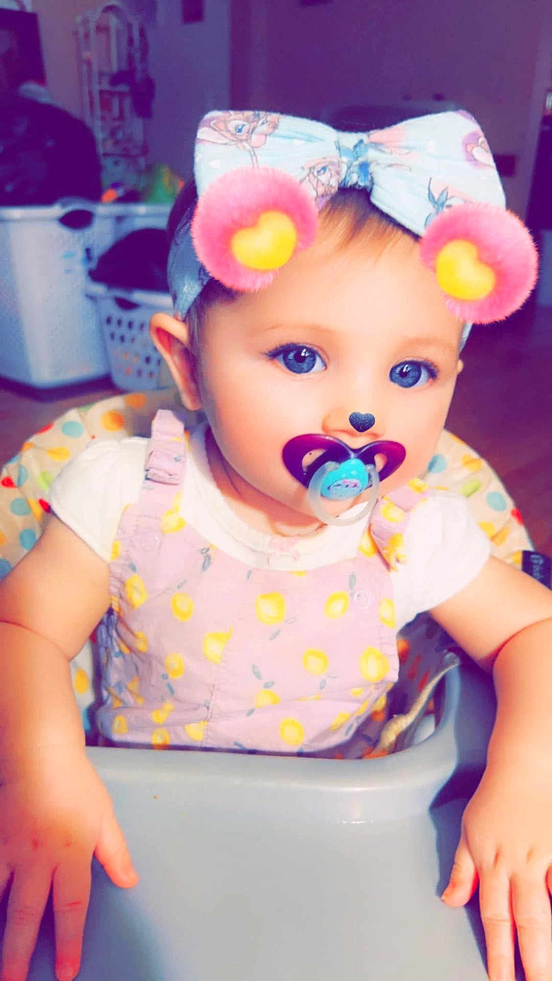 Bailey is registered to the contest to win money with this photo: baby, toddler, pacifier, headband, bow, high_chair, child, face, blue_eyes, hands, clothing, pink, white_shirt, patterned_outfit, indoor, digital_filter, cute, infant, playful, portrait