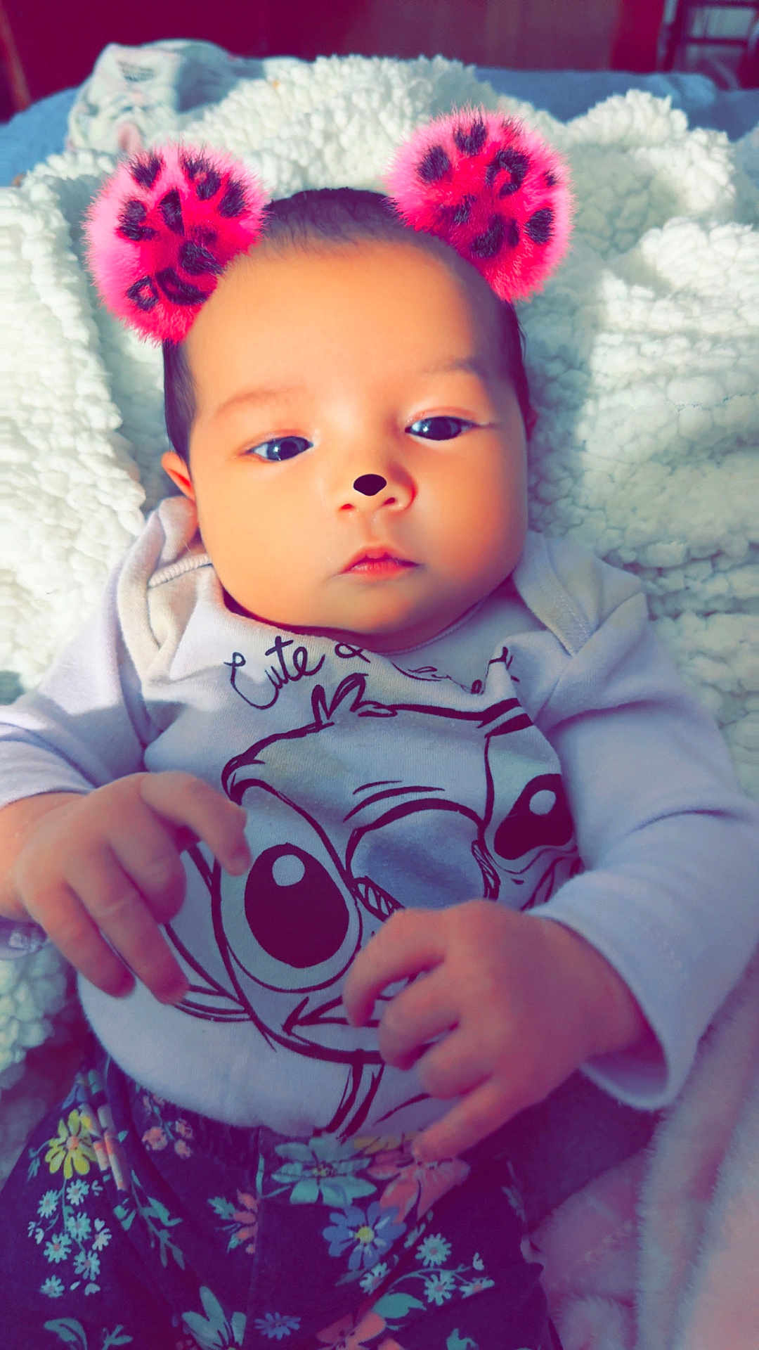 Sophia is registered to the contest to win money with this photo: baby, infant, face, hands, clothing, cartoon_print, floral_pants, blanket, cozy, cute, filter, pink_ears, nose, portrait, indoor, child, young, person, lying_down, soft