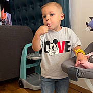 Nolan participe au concours pour gagner de l'argent avec cette photo : child, toddler, boy, lollipop, tshirt, mickey_mouse, love_text, jeans, sneakers, highchair, baby_seat, wooden_floor, standing, face, eyes, blond_hair, indoors, sofa, furniture, hand