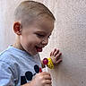 boy, candy, casual_clothing, child, face, haircut, hand, lollipop, playful, portrait, profile, short_hair, side_view, smiling, stucco_wall, t_shirt, toddler, tongue_out, watch, yellow_watch