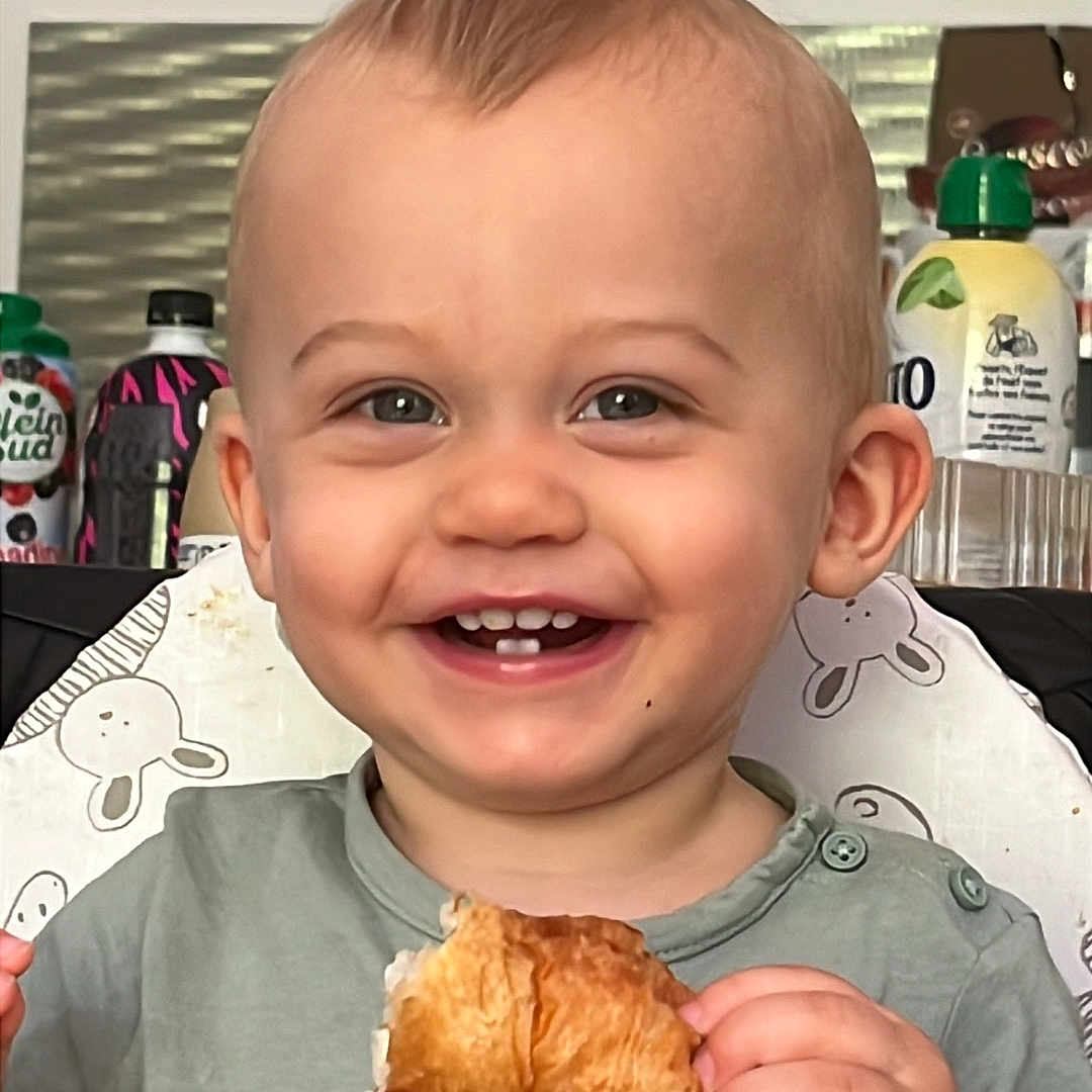 Giulliano a rejoint le concours — aidez-le/la à gagner de superbes lots ! background, bracelet, breakfast, child, clothing, croissant, cute, eating, face, food, hair, happy, highchair, indoor, kitchen, moawk, portrait, sitting, smiling, toddler