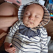 Anthony is registered to the contest to win money with this photo: baby, sleeping, hoodie, striped_clothing, whale_design, hand, face, closed_eyes, indoor, living_room, bookshelf, furniture, couch, blanket, person, child, relaxed, cute, peaceful, infant