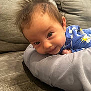 Noah joined the competition — help win amazing prizes! baby, child, infant, face, hair, couch, pillow, blue_clothing, smiling, cute, indoors, person, young_child, lying_down, soft_texture, curious, expression, comfortable, home, relaxed