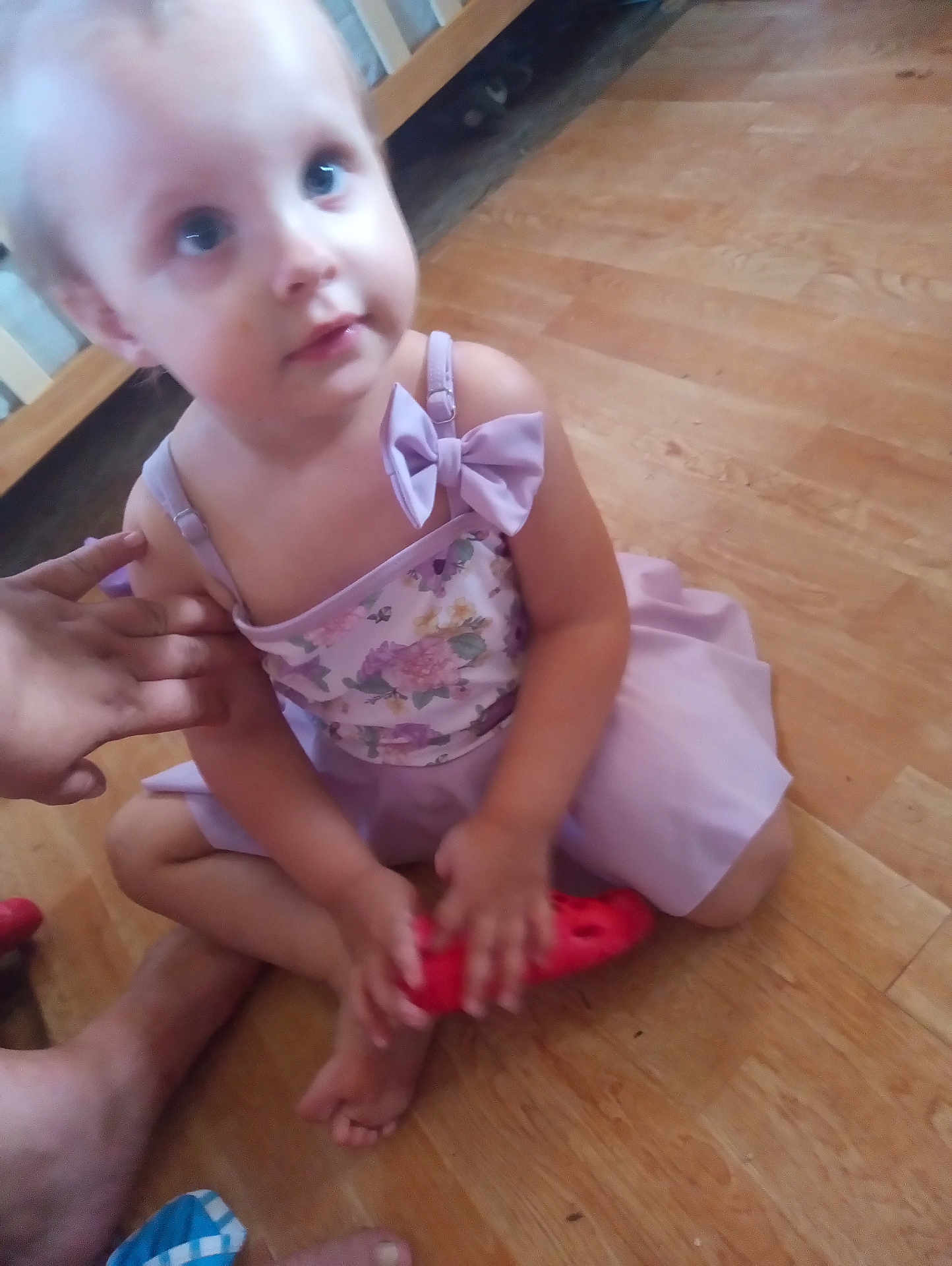 Freyja is registered to the contest to win money with this photo: child, toddler, dress, bow, floor, wooden_floor, toy, hand, barefoot, sitting, indoor, person, skin, face, blue_eyes, cute, young, small, holding, pink