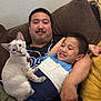 man, child, cat, couch, indoor, smiling, relaxed, brown_couch, white_cat, short_hair, casual_clothing, family, pet, home, comfort, furniture, cute, happy, resting, together