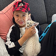 Luna joined the competition — help win amazing prizes! boy, cat, child, pet, smile, couch, pillow, cap, red_and_black, black_jacket, white_shirt, indoor, cozy, happy, cute, light_fur, blue_eyes, tablet, relaxing, affection