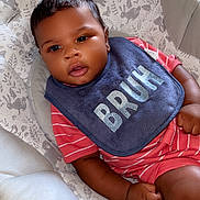 Adonis is registered to the contest to win money with this photo: baby, infant, bib, red_clothing, striped_clothing, seat, cushion, animal_pattern, face, hand, wooden_floor, indoor, curious_expression, child, cute, comfortable, soft_fabric, casual, portrait, young_child