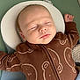 baby, sleeping, infant, onesie, brown_clothing, bear_pattern, face, cushion, baby_seat, peaceful, closed_eyes, arm, hand, soft_texture, head, portrait, child, resting, indoors, comfort