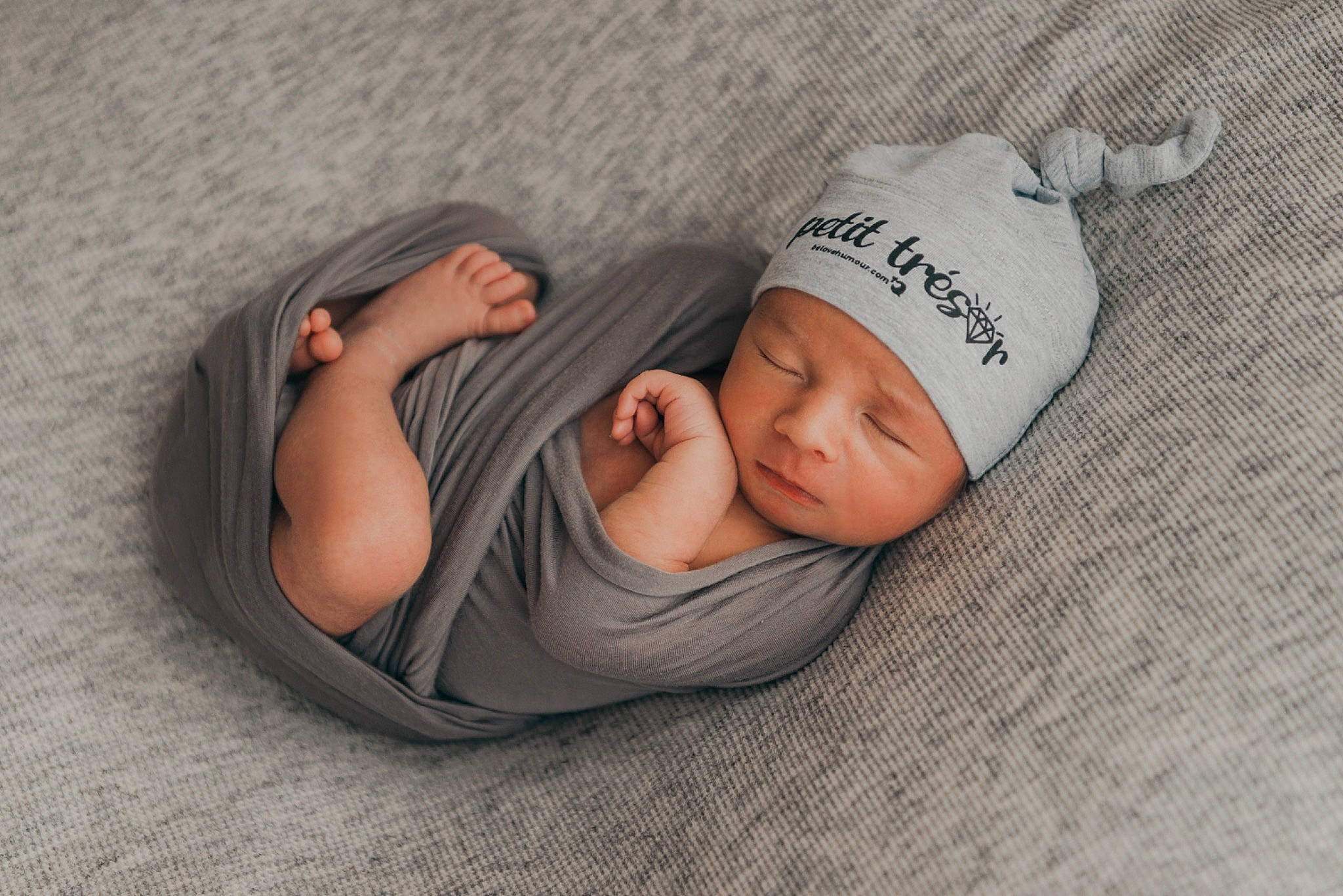 Logan participe au concours pour gagner de l'argent avec cette photo : baby, baby_products, baby_sleeping, baby_toddler_clothing, cap, child, comfort, face, finger, flooring, grey, hand, headgear, headwear, human_body, knit_cap, linens, person, product, skin
