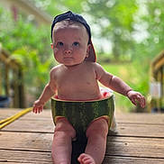 Cameron is registered to the contest to win money with this photo: baby, child, watermelon, hat, cap, outdoor, wooden_deck, greenery, summer, fruit, cute, sitting, portrait, skin, legs, feet, nature, daylight, expression, playful