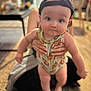 Cameron joined the competition — help win amazing prizes! baby, child, infant, person, cap, clothing, pretzel_pattern, hands, indoor, carpet, blurred_background, face, cute, close_up, holding, sitting, adult, floor, soft_lighting, expression