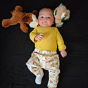 Ian joined the competition — help win amazing prizes! baby, child, infant, plush_toy, stuffed_animal, yellow_sweater, fox_patterned_pants, white_socks, lying_down, black_background, cute, soft_toys, portrait, childwear, indoors, calm_expression, playful, young_child, small_hands, cozy