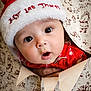 adorable, baby, celebration, child, christmas, closeup, cute, expression, face, festive, holiday, holiday_season, infant, present, red_clothing, santa_hat, surprised, unwrapping, wide_eyes, wrapping_paper