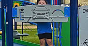 Amelia joined the competition — help win amazing prizes! child, playground, play_equipment, blue, green, shorts, sneakers, grass, outdoor, person, park, daylight, fun, curly_hair, panel, car_drawing, legs, standing, smiling, metal_structure