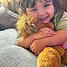 Amelia joined the competition — help win amazing prizes! child, smiling, curly_hair, stuffed_animal, lion, hugging, couch, gray, cozy, indoors, natural_light, happy, cute, portrait, young_child, toy, plush, relaxed, home, person