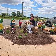 Amelia is registered to the contest to win money with this photo: child, statue, deer, gnome, garden, outdoor, sky, clouds, vehicle, greenery, plants, mulch, sidewalk, playful, happy, sculpture, nature, park, daytime, casual
