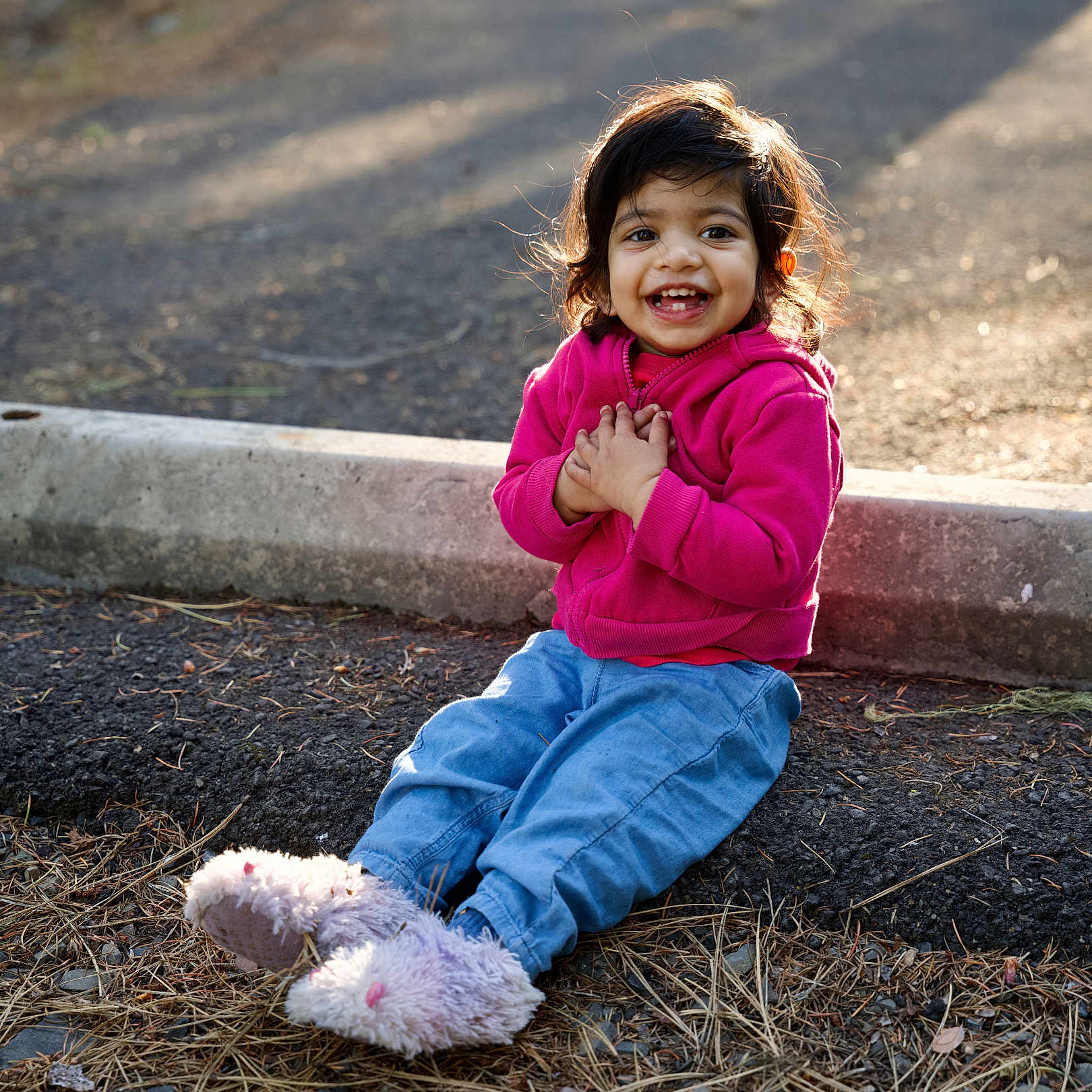 Nidhira Avirneni joined the competition — help win amazing prizes! blue_pants, casual_clothing, child, curb, cute, daylight, fluffy_slippers, grass, ground, happy, hoodie, nature, outdoor, pine_needles, pink_clothing, portrait, sitting, smile, sunlight, toddler