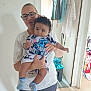 Aaron participe au concours pour gagner de l'argent avec cette photo : adult, baby, child, glasses, indoor, doorway, clothing, socks, person, holding, curly_hair, white_shirt, striped_socks, cartoon_print, household_items, laundry, floor, door, smile, casual