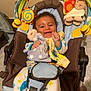 Aaron a rejoint le concours — aidez-le/la à gagner de superbes lots ! baby, smiling, infant, toy, baby_seat, colorful, plush_toy, hanging_toy, clothing, bibs, indoor, happy, cute, child, person, seatbelt, fabric, patterned_clothing, curly_hair, playful