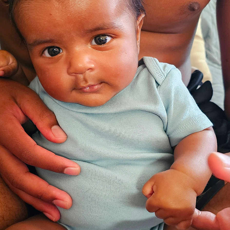 Nisaiah joined the competition — help win amazing prizes! adult, baby, closeup, clothing, cute, expression, eyes, face, fingers, hand, holding, human, indoor, infant, legs, onesie, person, portrait, skin, tattoo