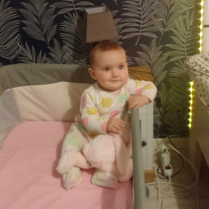 Mia Gadouche a rejoint le concours — aidez-le/la à gagner de superbes lots ! baby, baby_clothes, blanket, carpet, child, cozy, crawling, floor, furniture, home, indoor, lamp, nursery, person, playpen, plush_toy, smiling, soft_lighting, toy, wallpaper