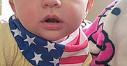 Caspian joined the competition — help win amazing prizes! baby, bed, bib, blanket, candid, closeup, curious, eyes, face, flag, hand, hello_kitty, indoor, infant, plush_toy, portrait, stars, stripes, yellow_shirt, young_child
