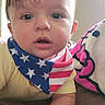 american_flag, baby, bandana, bed, blanket, child, clothing, cute, expression, eyes, face, hair, hand, head, indoor, infant, mouth, person, portrait, skin