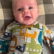 Lennox joined the competition — help win amazing prizes! baby, infant, smiling, face, onesie, clothing, pattern, airplane_print, pillow, checkered, fabric, happy, cute, child, person, lying_down, indoors, closeup, portrait, drool